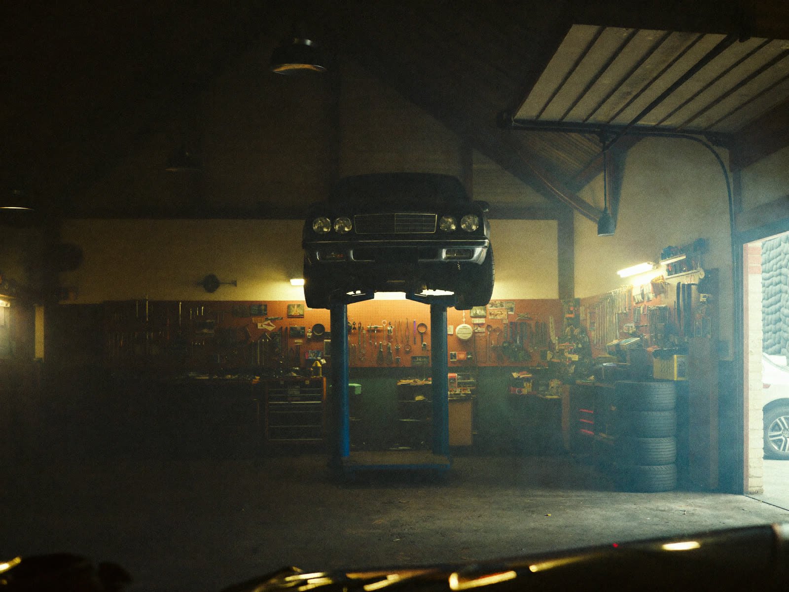 Interior del taller con un auto elevado y herramientas en la pared