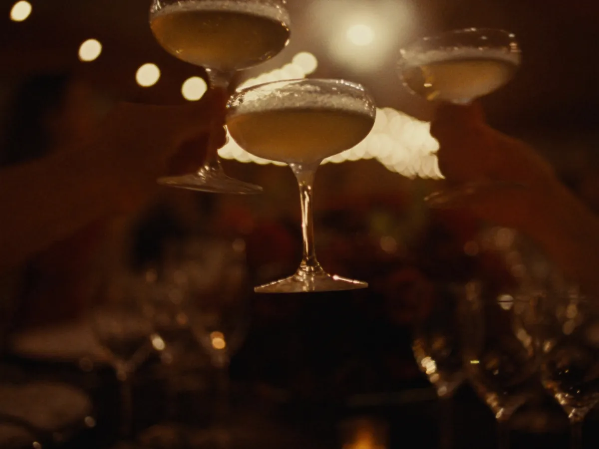 Copas de brindis sobre una mesa con flores bordó y luces cálidas de fondo