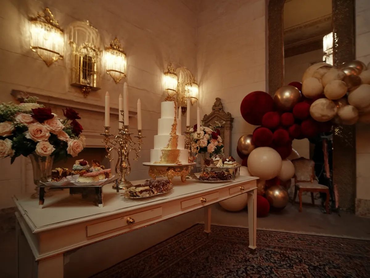 Mesa dulce para cumpleaños formal con torta dorada, candelabros y guirnalda de globos bordó y dorado