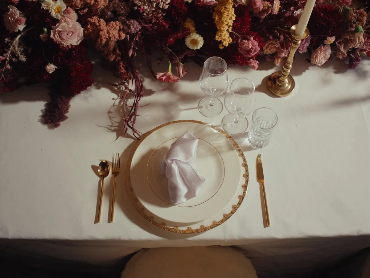 Detalle de mesa principal con flores en tonos rosados y bordó, vajilla dorada y copas de cristal