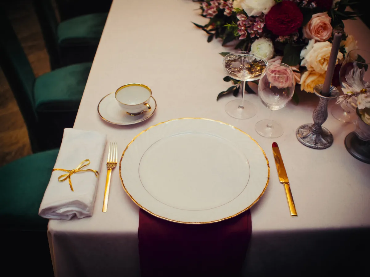 Detalle de mesa de Villa Aurelia con vajilla de borde dorado, copas de cristal y centro floral bordó